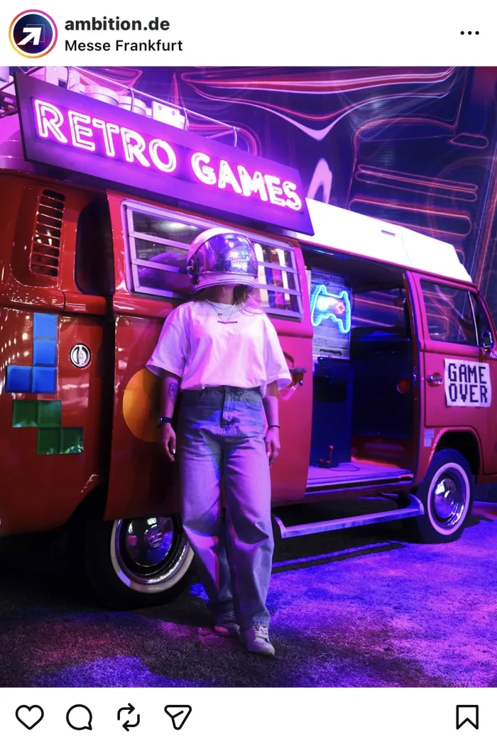 Besucherin mit Helm vor dem Retro-Games-Bus mit Leuchtschrift auf der AMBITION