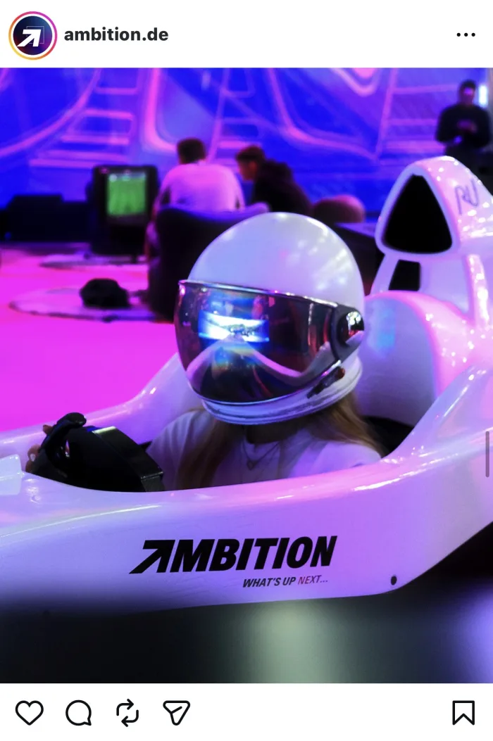 Besucherin mit verspiegeltem Helm im AMBITION-Rennsimulator, im Hintergrund die Gaming-Fläche
